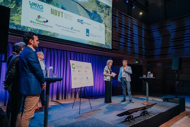 WebBT0624KRDVHS5a | BouwTotaal Mensen op een podium tijdens een conferentie met presentatiescherm en sprekers.