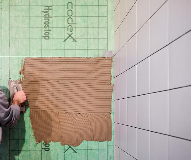 Werkman brengt mortel aan op een waterdichte groene afdichtings- en ontkoppelingsman naast een betegelde muur