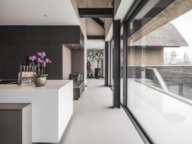 Lichte moderne woonkamer met grote ramen, wit kookeiland, en zicht op buiten.