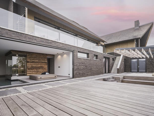 Moderne buitenruimte met houten terras, grindtuin en overdekte lounge naast een huis met donkere gevel.