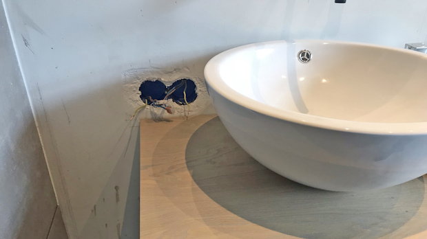 Wastafel met onafgewerkte leidingdoorvoer in een badkamer die door een onervaren klusser is gerenoveerd.