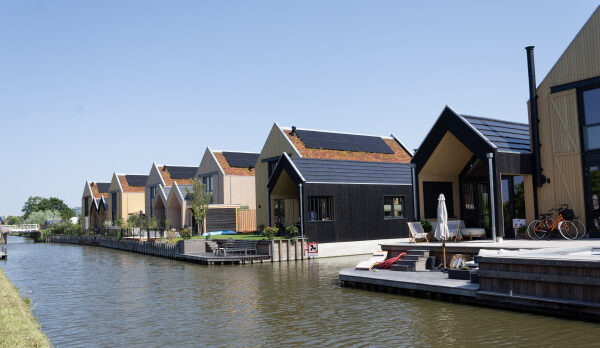 Row of modern, peaked-roof houses along a canal with wooden decks and outdoor seating by the water